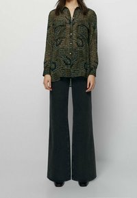 Loose, patterned, dark green blouse with long sleeves and button front, paired with wide-leg, high-waisted black jeans.