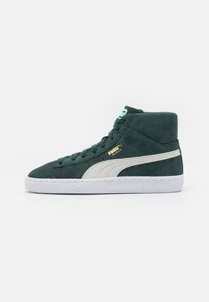 Ciemnozielony zamszowy trampki Puma za kostkę z białym paskiem, białą podeszwą, zieloną metką na języku i złotym napisem „PUMA SUEDE” po boku.