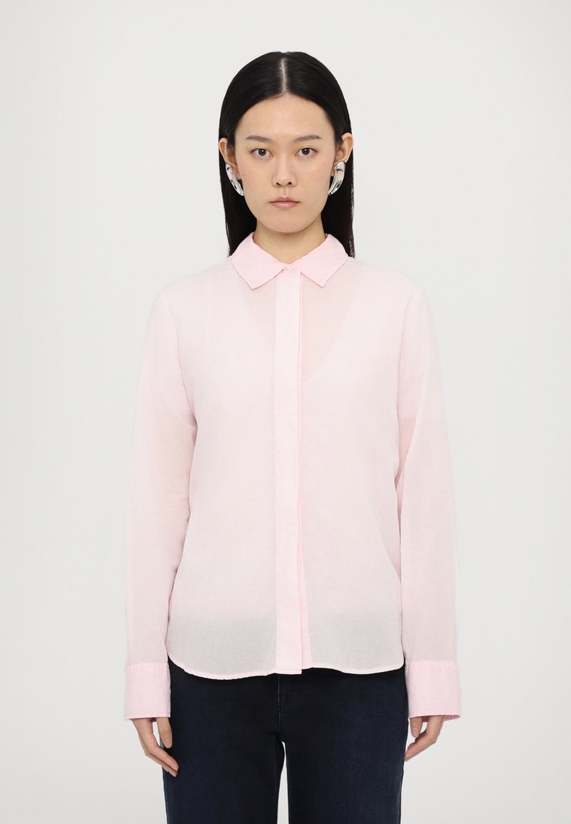 Chemise à manches longues rose clair avec une fermeture à boutons à l'avant, un col et une texture douce. Présente un matériau légèrement transparent et un design simple.