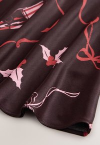Tissu foncé à texture lisse présentant un motif de feuilles de houx rouges et de rubans roses. L'ourlet incurvé met en valeur des détails de design complexes.