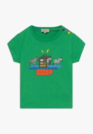 Camiseta verde para niño pequeño con mangas cortas, botones a presión en el hombro y gráfico de cebras que cambian de color en una cinta transportadora.