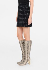 Stivali al ginocchio in stampa pitone dorato con tacco a blocco, abbinati a una mini gonna nera in tweed con motivo a griglia e dettaglio dei bottoni.