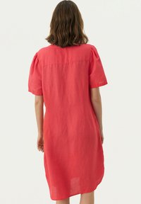 Rosa Leinenkleid mit kurzen Puffärmeln, lockerer Passform und geradem Saum. Nahtdetails entlang des Rückens und ein minimalistisches Design.