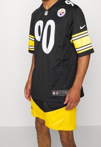 Maillot noir de la NFL avec de grands chiffres blancs, des manches rayées jaunes et un logo cousu ; associé à des shorts noirs et jaunes pour une tenue de sport.
