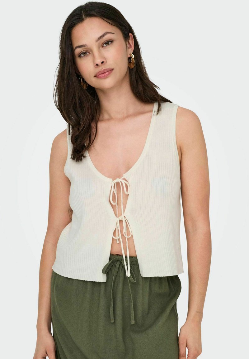 Geverfd ivoorkleurig topje met een diepe V-hals en een striksluiting aan de voorkant, gecombineerd met een groene hoog-waist rok. Gladde textuur, casual stijl.