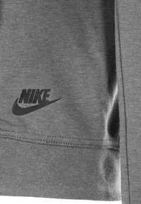 Grå Nike-huvtröja med en mjuk textur, ribbad nederkant och en svart logotyp tryckt på vänster sida nära sömmen.