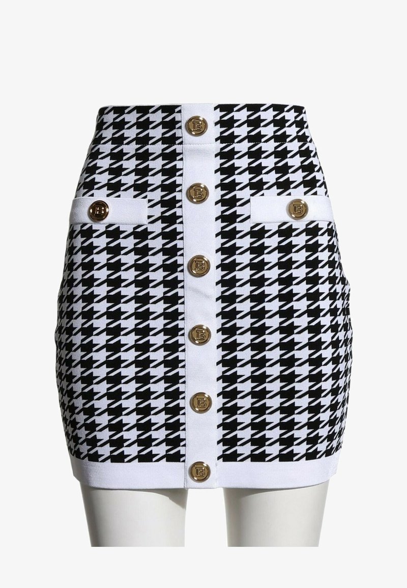 Mini-jupe pied-de-poule noir et blanc avec bordure blanche, boutons dorés au centre et deux pattes décoratives boutonnées aux hanches.