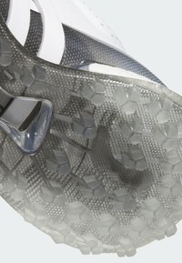 Przezroczysta podeszwa z teksturowanym sześciokątnym wzorem; biała cholewka z szarymi akcentami; smukły design przeznaczony do użytku sportowego.