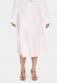 Jupe midi en satin rose pâle avec une texture lisse et une silhouette évasée, associée à des sandales à lanières oliviers. Design léger et fluide.