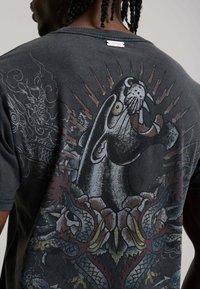 Man wearing a dark shirt with a large graphic of a roaring panther surrounded by stylized dragons and spikes on the back.