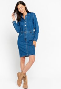 Denim srajčna obleka s ovratnikom, z gumbi spredaj, oprijetim pasom in dvema stranskima žepoma. Nosimo jo z rjavimi čipkastimi gležnjarji.