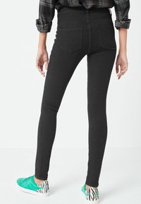 Černé skinny džíny s vysokým pasem a hladkým povrchem, se dvěma zadními kapsami, doplněné zelenými teniskami se zebrovým vzorem na patě.