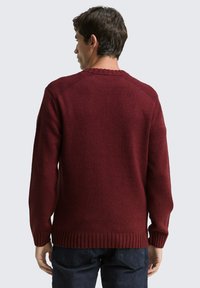 Weinroter Strickpullover mit rundem Ausschnitt, geripptem Saum und Bündchen sowie strukturierter Rückseite. Der Stoff scheint weich zu sein und hat eine enge Passform.