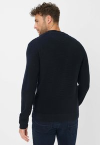 Marineblauwe ronde hals trui van textuur gebreid stof, met lange mouwen en een geribbelde rand, gecombineerd met donkere spijkerbroeken.