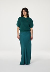 Teal gebreide trui met korte, poffende mouwen, gecombineerd met een lange, getailleerde teal satijnen rok. Opvallend detail: kleine zwarte versiering op de trui.