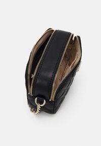 Borsa a tracolla nera trapuntata in pelle con due scomparti con zip, hardware dorato e un dettaglio in catena laterale. Interno color beige.