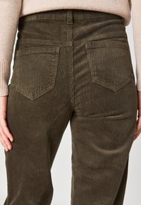 Pantalons en velours côtelé vert olive avec une texture à côtes verticales, dotés de deux poches arrière et d'une taille haute.