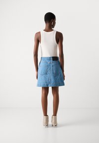 Jeanskjørt med en utvidet fasong, lys blå farge, frynset kant og to baklommer. Kombinert med et tettsittende hvitt topp og beige ankelstøvler.