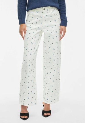 Model wearing white wide-leg pants with blue floral patterns, paired with a navy sweater and black open-toe heels.