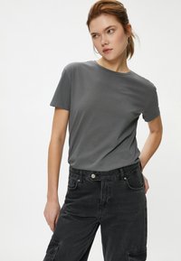 T-shirt en coton gris à manches courtes et à col rond, associé à un pantalon cargo en denim noir taille haute avec des poches latérales.