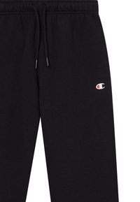 Schwarze Jogginghose mit elastischem Bund, schwarzen Kordeln und kleinem weißen und roten Champion-Logo am Oberschenkel.