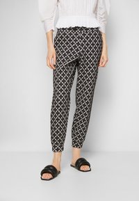 Svartvita mönstrade byxor med en diamantkorsdesign, smal passform och elastisk midja, i kombination med svarta slidesandaler.