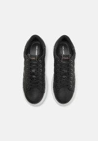 Svarta lädersneakers med en texturerad ovandel, vit gummisula och kontrasterande snören; har en logotypdetalj nära snörena.