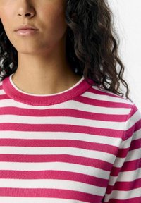 Pull rayé avec des lignes horizontales rose et blanche, présentant un col rond côtelé et une texture tricotée douce. Détails visibles sur les coutures des épaules.
