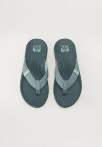 Lyseblå flip-flops med teksturerte såler og bred stropp. Designet inkluderer en tommelpost og detaljer på den øvre stroppen.
