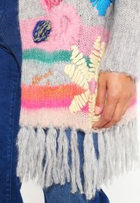 Écharpe tricotée avec des rayures multicolores en rose, vert et gris, ornée de broderies florales et de détails en franges grises en bas.