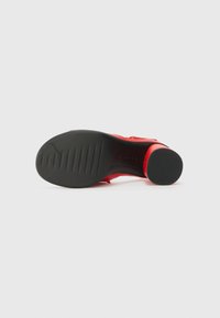 Red leather sandal with a wide strap, a rounded toe, and a textured black rubber sole featuring horizontal grooves and a round heel.
