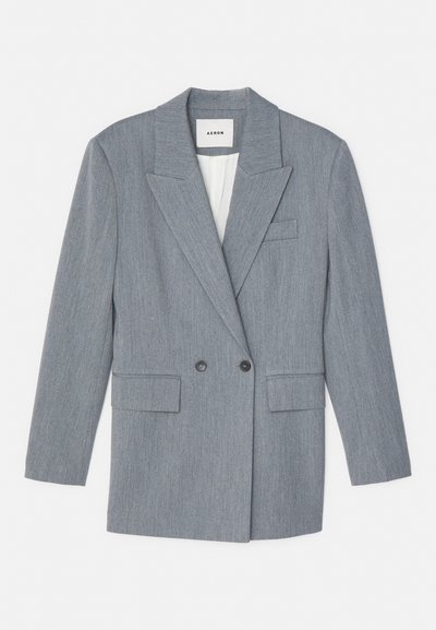 Sivina, prilagojena blazer jakna, izdelana iz teksturiranega materiala. Ima dvojno zadrgo, zareznimi ozkimi ovratniki in dvema sprednjima žepoma.