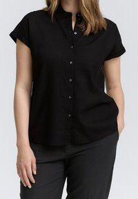 Camicia nera a maniche corte con bottoni, caratterizzata da un colletto, una vestibilità dritta, una texture morbida e piccoli bottoni neri lungo la pattina frontale.