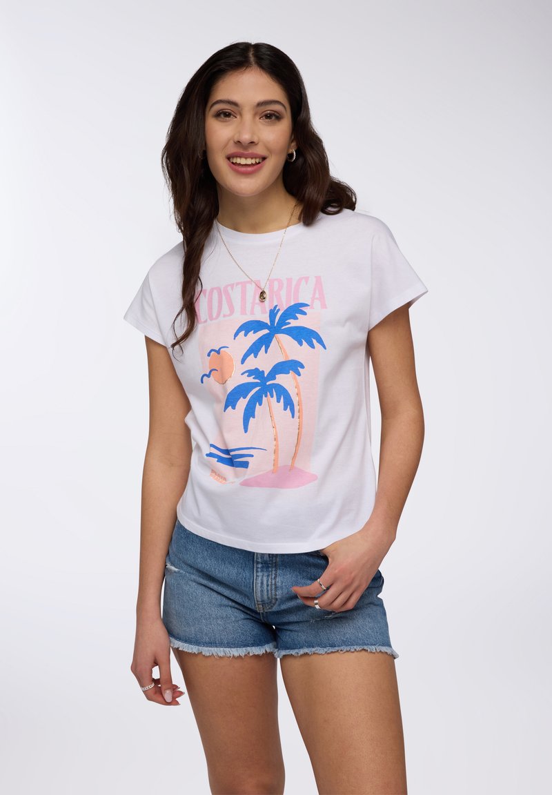 T-shirt bianco a maniche corte con grafica "COSTA RICA" in rosa e blu, che presenta palme e un tramonto. Indossato con pantaloni corti in denim azzurro chiaro.