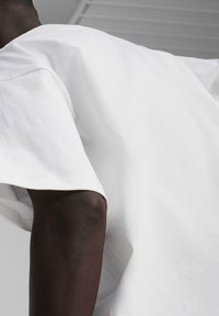 Hvid bomulds T-shirt med afslappet pasform, der har korte ærmer og minimale sømme, mod en lys grå baggrund.