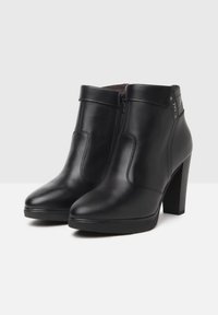Bottines en cuir noir avec une finition lisse, bout pointu, fermeture éclair latérale et un talon haut texturé. Design simple avec des accents de matériel minimal.