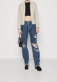 Beżowa marynarka na czarnym topie odsłaniającym brzuch, zestawiona z podniszczonymi niebieskimi jeansami z przetarciami i postrzępionymi nogawkami. Czarna mini torebka i masywne buty.