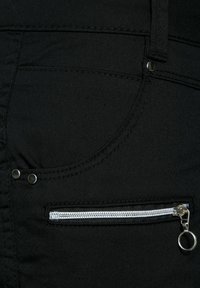 Tessuto di denim nero con una tasca frontale dotata di chiusura lampo argentata e un piccolo tirante circolare. Due rivetti metallici vicino alla tasca.