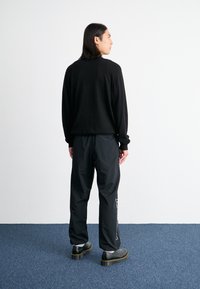Black long-sleeve sweater and black loose pants with an embroidered detail. Worn with platform shoes, viewed from the back.