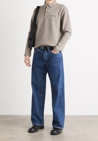 Person wearing beige long-sleeve polo with "BOSS" logo, blue wide-leg jeans, black belt, black shoes, and carrying a black shoulder bag.