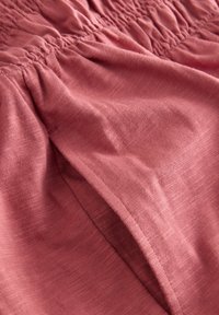 Tessuto morbido rosa polvere con cucitura elastica raccolta vicino al bordo superiore, che mostra una trama liscia e dettagli fini della tessitura.