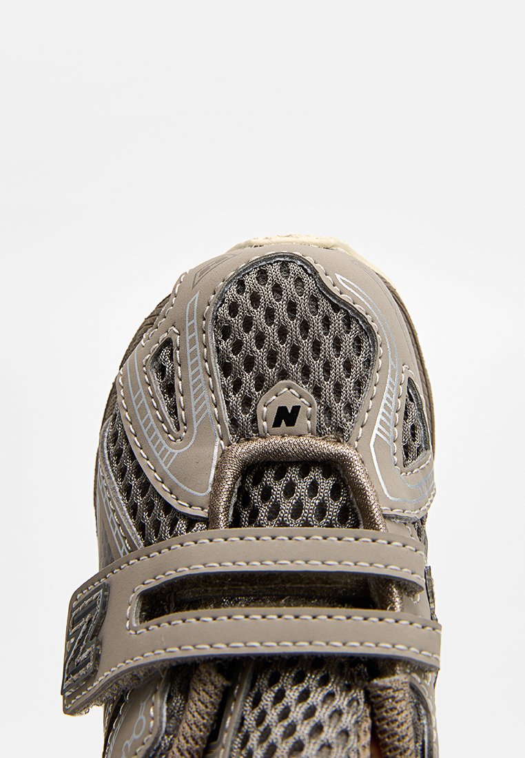 Chaussure de sport légère grise avec une tige en mesh, un col rembourré et une sangle à boucle. Présente des coutures contrastantes et une semelle en caoutchouc.