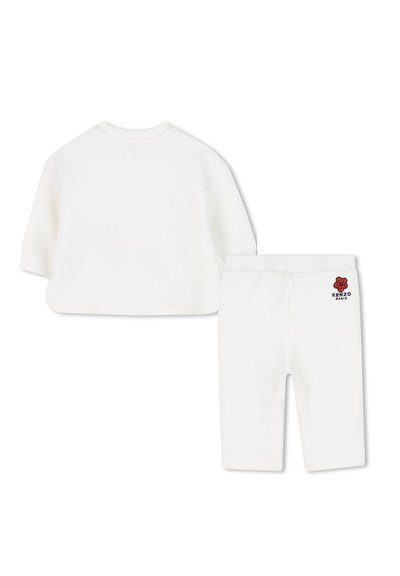 Ensemble tricoté blanc pour tout-petit composé d'un haut à manches courtes et d'un pantalon assorti, orné d'un logo de fleur rouge sur la cuisse gauche.