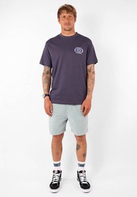 T-shirt à manches courtes violet foncé avec un motif floral sur la poitrine gauche, associé à un short bleu clair et des baskets montantes noires.
