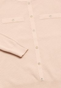 Jasnoróżowy sweter z dzianiny z teksturowanym wzorem, okrągłym dekoltem, zapięciem na guziki z ozdobnymi akcentami oraz dwiema kieszeniami na piersi.