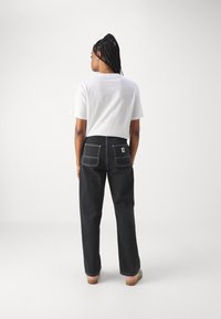 Μαύρο τζιν παντελόνι με λευκή ραφή, δύο πίσω τσέπες. Φορεμένο με λευκό μπλουζάκι και πολύχρωμα παπούτσια, από πίσω.