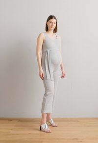 Grå graviditetsbuksedress med en tettsittende design, knytebelte i midjen og vide ben, kombinert med metalliske hælsandaler. Glatt stofftekstur.