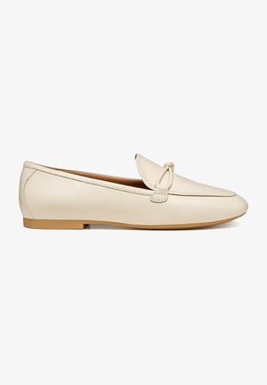 Mocassins en cuir beige avec un bout arrondi et un nœud décoratif sur le dessus. Semelle plate en caoutchouc avec un détail de couture minimal.
