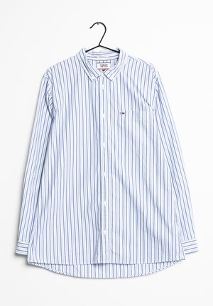 Chemise pour homme à manches longues avec des rayures verticales bleues et blanches, une petite poche poitrine et un col, suspendue à un cintre noir.