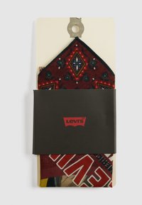 Fazzoletto da taschino bordeaux con motivo piegato su cartoncino beige con fascia nera del logo Levi's su sfondo bianco.
